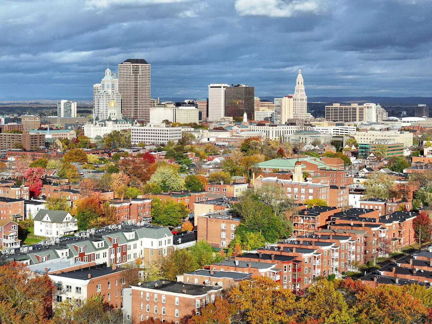 Aerial view of downtown Hartford, Connecticut skyline with the Travelers Tower and State Capitol dome, surrounded by brick residential neighborhoods in autumn
