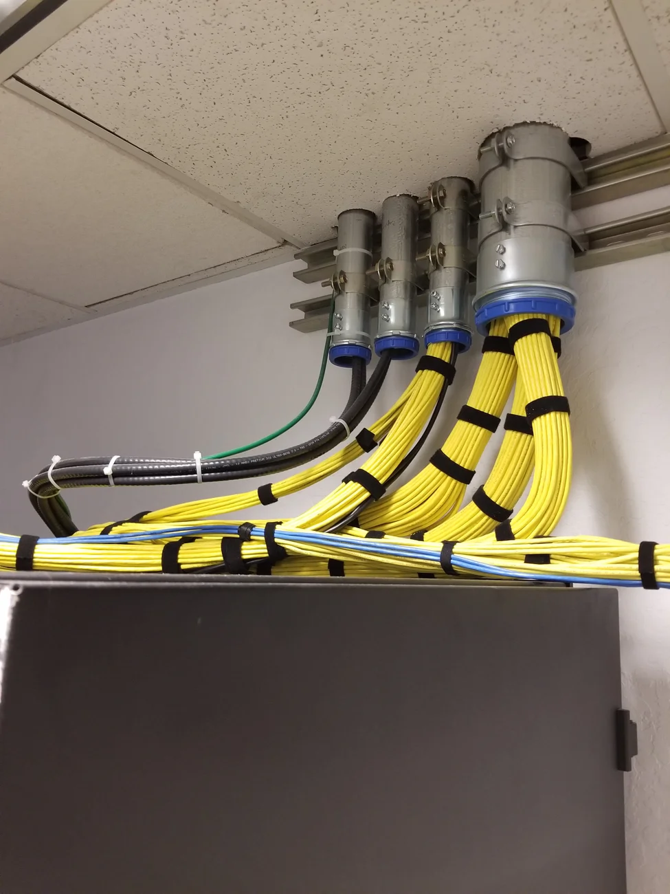 Field photograph of bundled cables entering conduit above an equipment cabinet